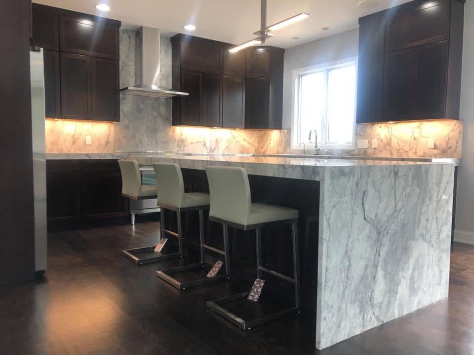 Marble waterfall island with bar seating in a dark-cabinet kitchen
